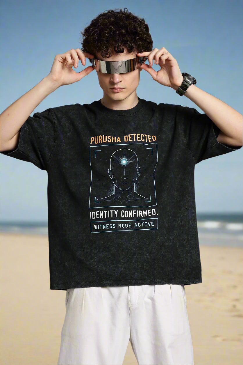 Oversized acid wash black T-shirt with “Purusha Detected” text. Inspired by Vedic philosophy, in dark grey charcoal tones for a bold, streetwear look.