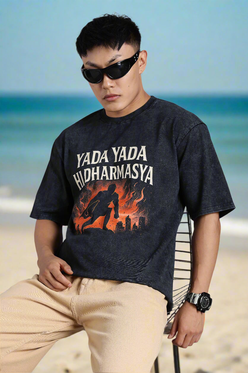 Person wearing a black t-shirt with graphic design and text, sitting on a chair against a gray background